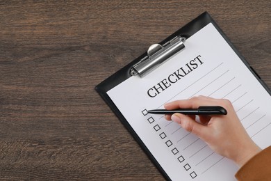 Woman filling Checklist at wooden table, top view. Space for text