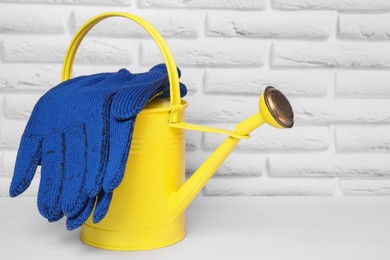 Photo of Yellow watering can with gardening gloves on white wooden table
