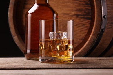 Photo of Whiskey with ice cubes in glass, bottle and barrel on wooden table