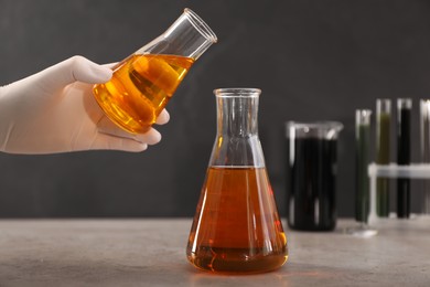 Woman pouring yellow crude oil into flask at grey table, closeup