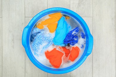 Photo of Basin with colorful clothes on floor, top view. Hand washing laundry