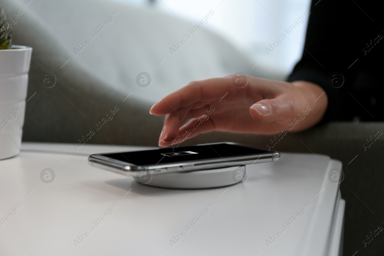 Photo of Woman taking smartphone from wireless charger in room, closeup
