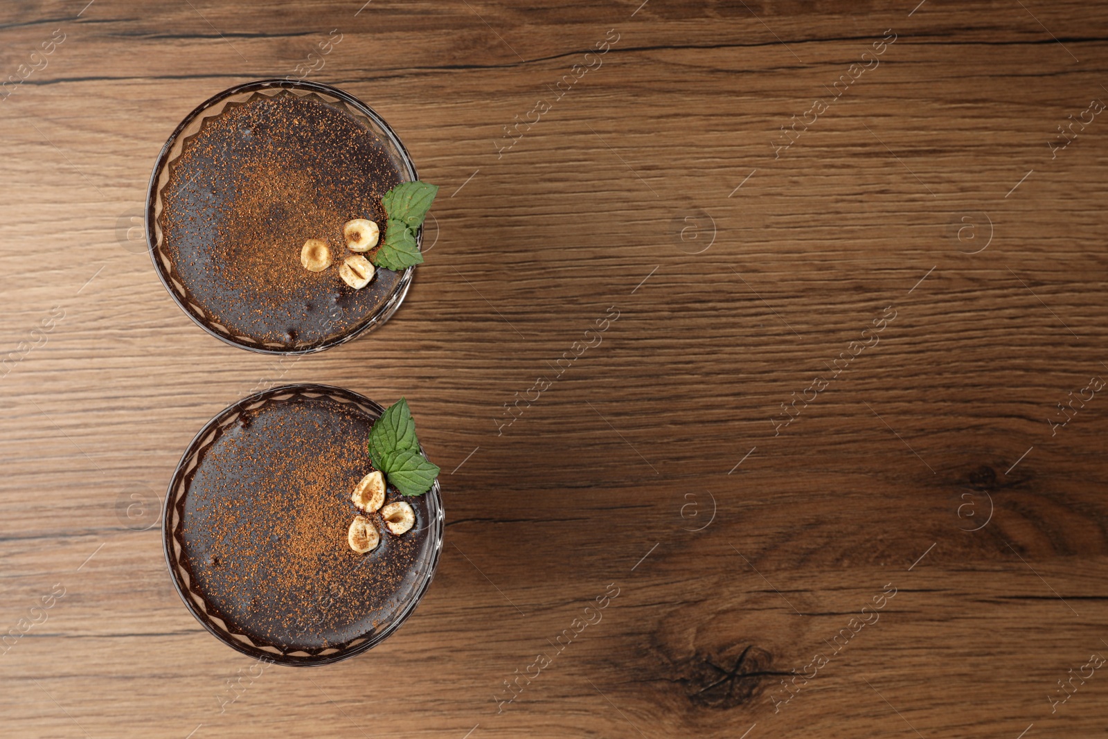 Photo of Dessert bowls of delicious hot chocolate with hazelnuts and fresh mint on wooden table, flat lay. Space for text