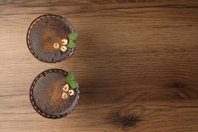 Photo of Dessert bowls of delicious hot chocolate with hazelnuts and fresh mint on wooden table, flat lay. Space for text