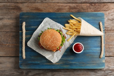 Photo of Tasty burger, french fries and sauce on wooden board, top view