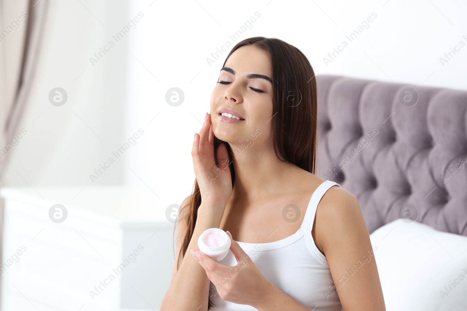 Photo of Young woman with jar of cream in bedroom. Beauty and body care