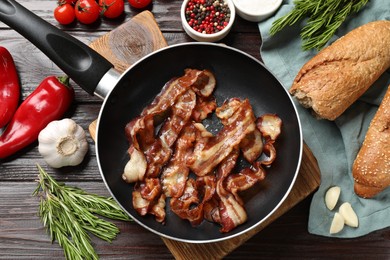 Delicious bacon slices in frying pan and products on wooden table, flat lay