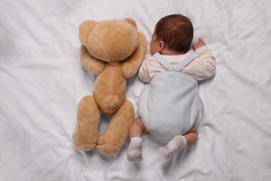 Photo of Newborn baby sleeping with toy bear on white blanket, top view