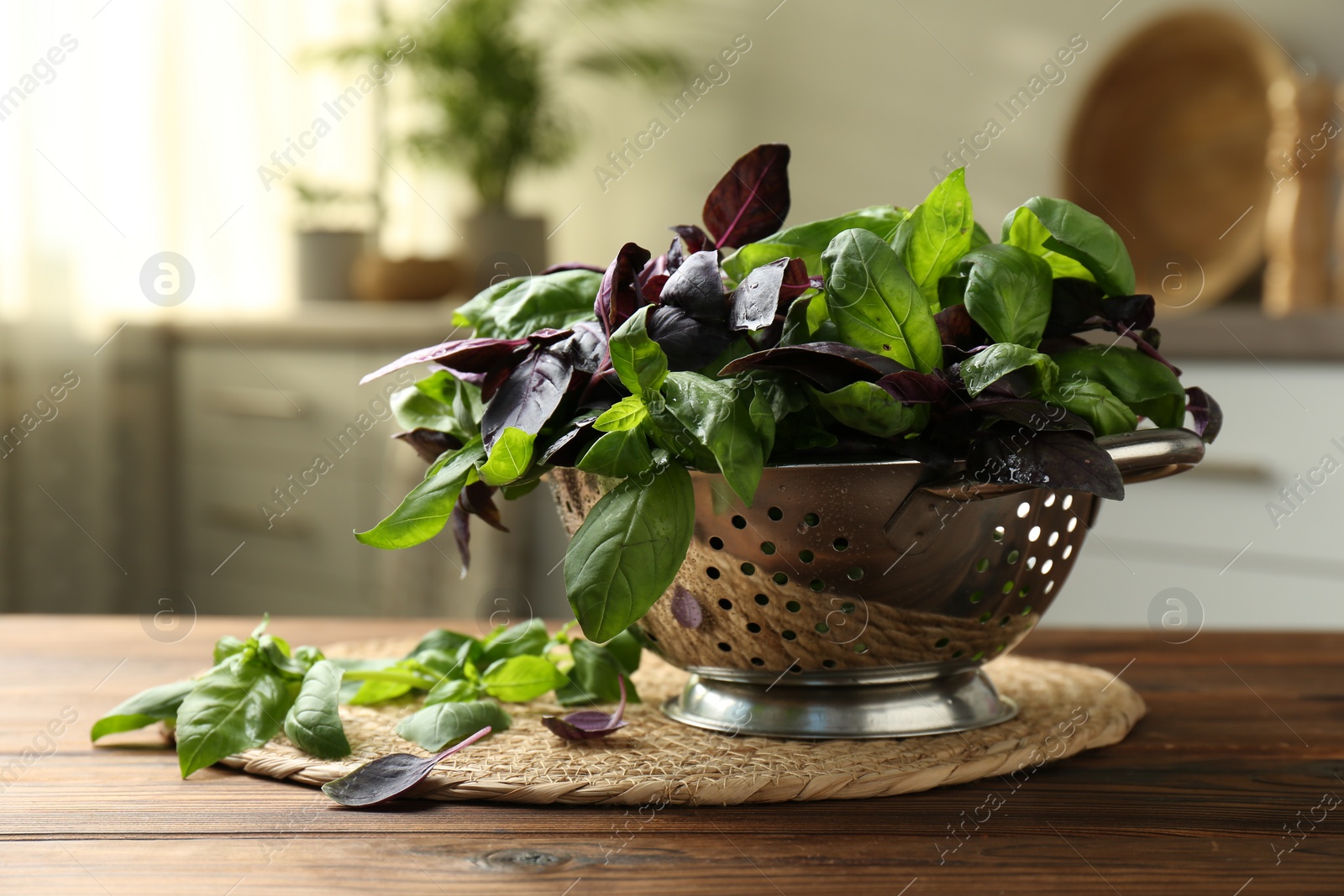 Photo of Metal colander with different fresh basil leaves on wooden table in kitchen