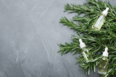 Fresh rosemary and bottles of essential oil on grey table, flat lay. Space for text