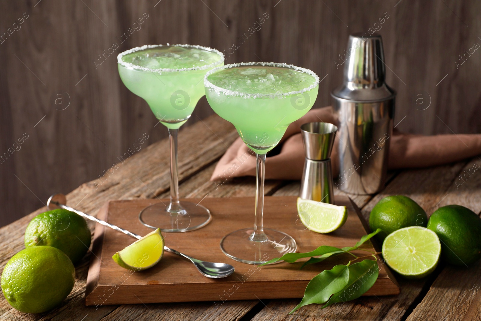 Photo of Delicious Margarita cocktail in glasses, limes and bartender equipment on wooden table