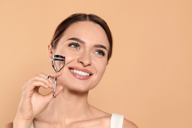 Woman with eyelash curler on beige background, space for text