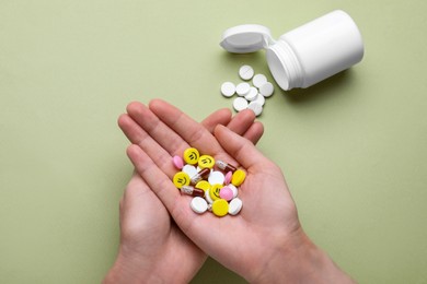 Woman holding colorful antidepressants on light green background, top view