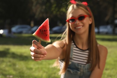 Photo of Beautiful girl with piece of watermelon in park, focus on hand