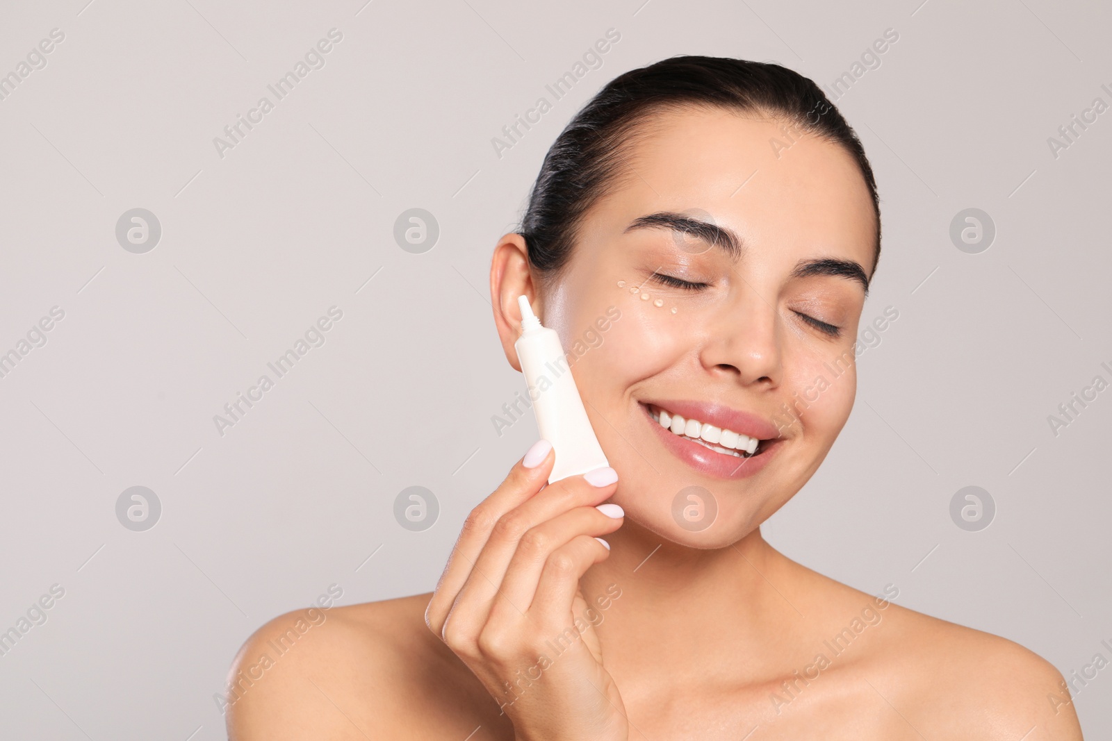 Photo of Beautiful young woman with gel on skin under eye against light grey background, space for text