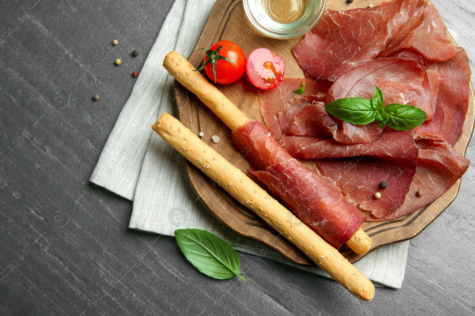 Photo of Delicious bresaola, tomato, grissini sticks and basil leaves on grey textured table, top view. Space for text