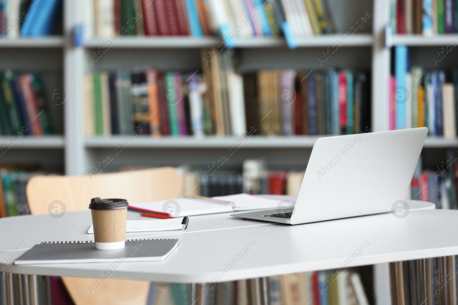 Photo of Laptop, drink and stationery on table in library