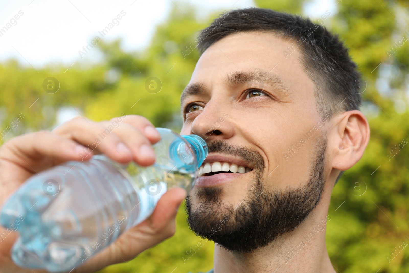 Photo of Happy man drinking water outdoors on hot summer day. Refreshing drink