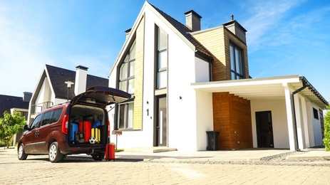 Car with suitcases in trunk near modern house outdoors. Moving day