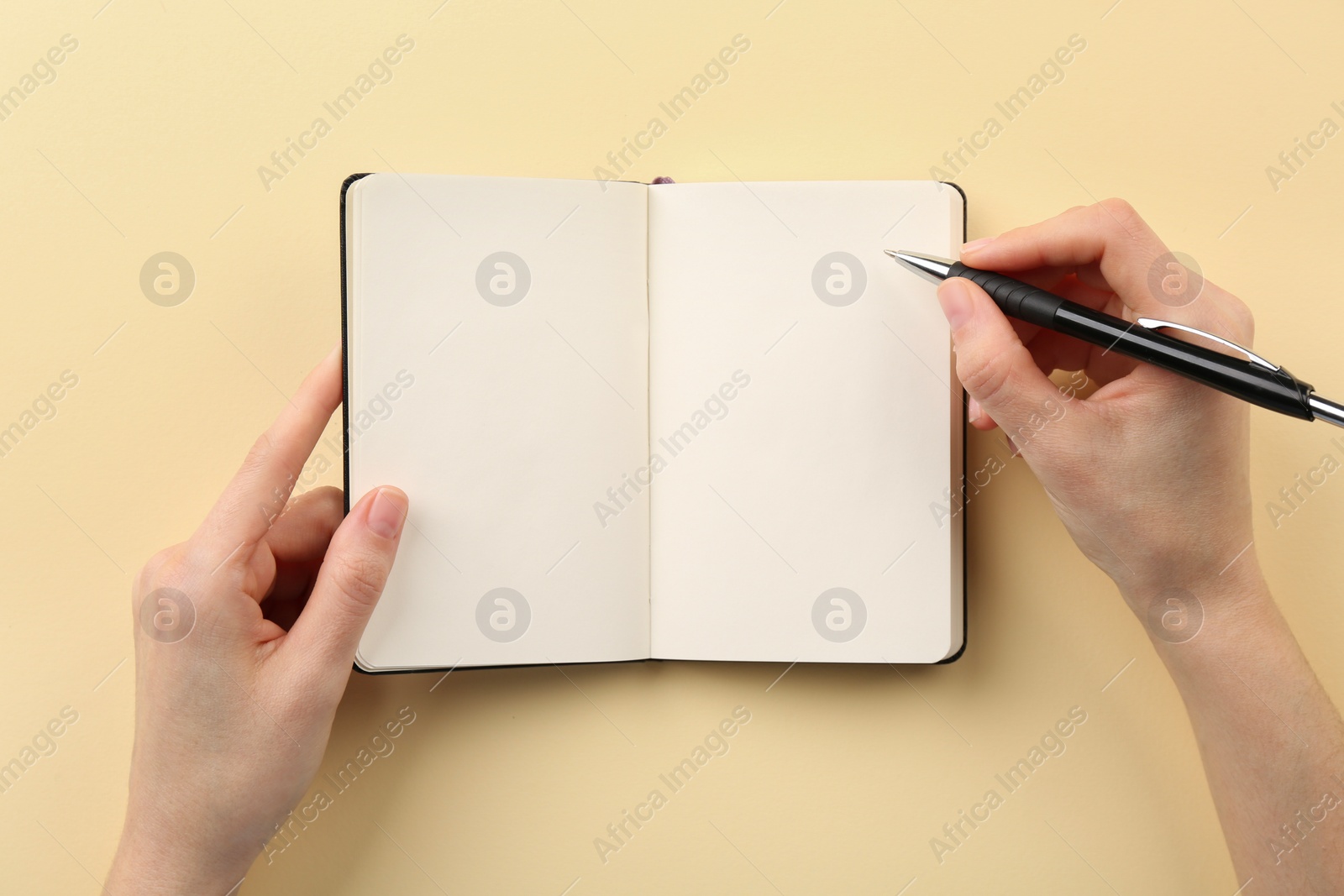 Photo of Woman writing in notebook on beige background, top view