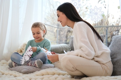 Mother and daughter making paper snowflakes near window at home