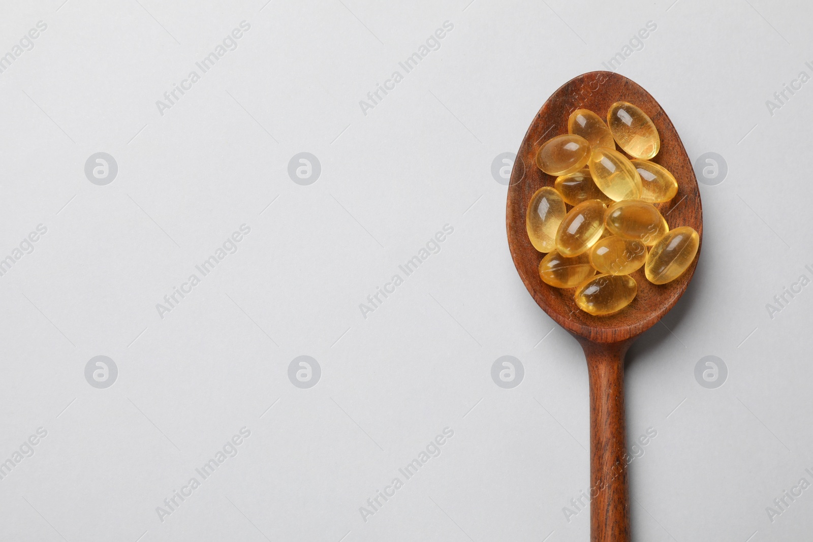 Photo of Vitamin capsules in wooden spoon on light grey background, top view. Space for text