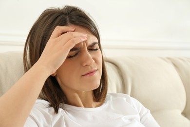 Photo of Young woman suffering from migraine on sofa at home