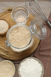 Leaven, ears of wheat, whisk, water and flour on beige wooden table, flat lay