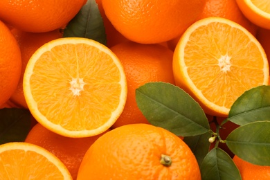 Cut and whole fresh ripe oranges with green leaves as background, top view