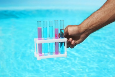 Photo of Man holding test tubes with reagents near swimming pool, closeup