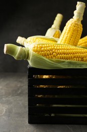 Photo of Wooden crate with tasty fresh corn cobs on grey table