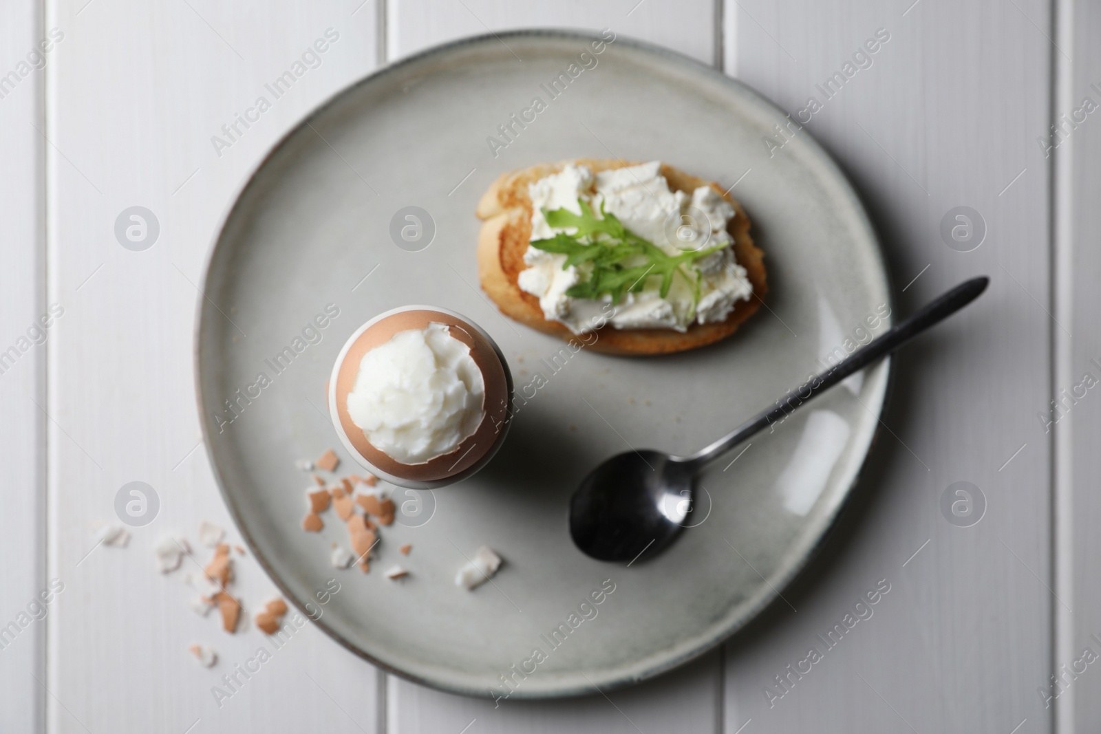 Photo of Fresh soft boiled egg in cup and sandwich on white wooden table, top view