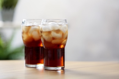 Photo of Glasses of cola with ice on table against blurred background, space for text