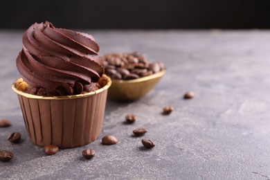 Photo of Delicious chocolate cupcake and coffee beans on grey textured table, closeup. Space for text