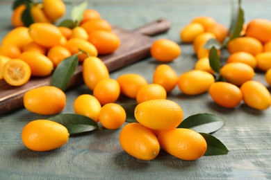 Photo of Fresh ripe kumquats and leaves on light blue wooden table