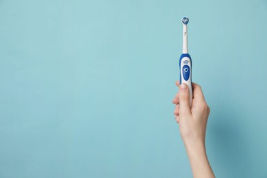 Woman holding electric toothbrush on light blue background, closeup. Space for text