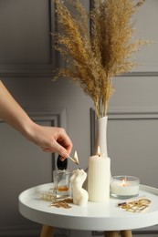 Photo of Woman lighting female body shaped candle on white table, closeup. Stylish decor