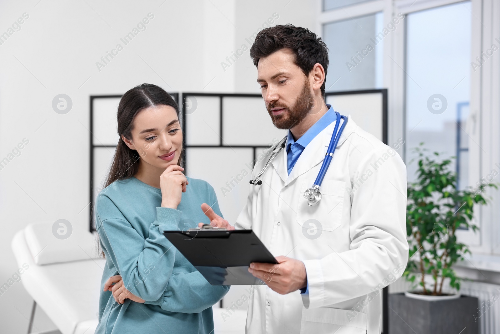 Photo of Doctor with clipboard consulting patient during appointment in clinic