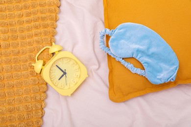 Photo of Light blue sleep mask, pillow and alarm clock on beige cloth, flat lay