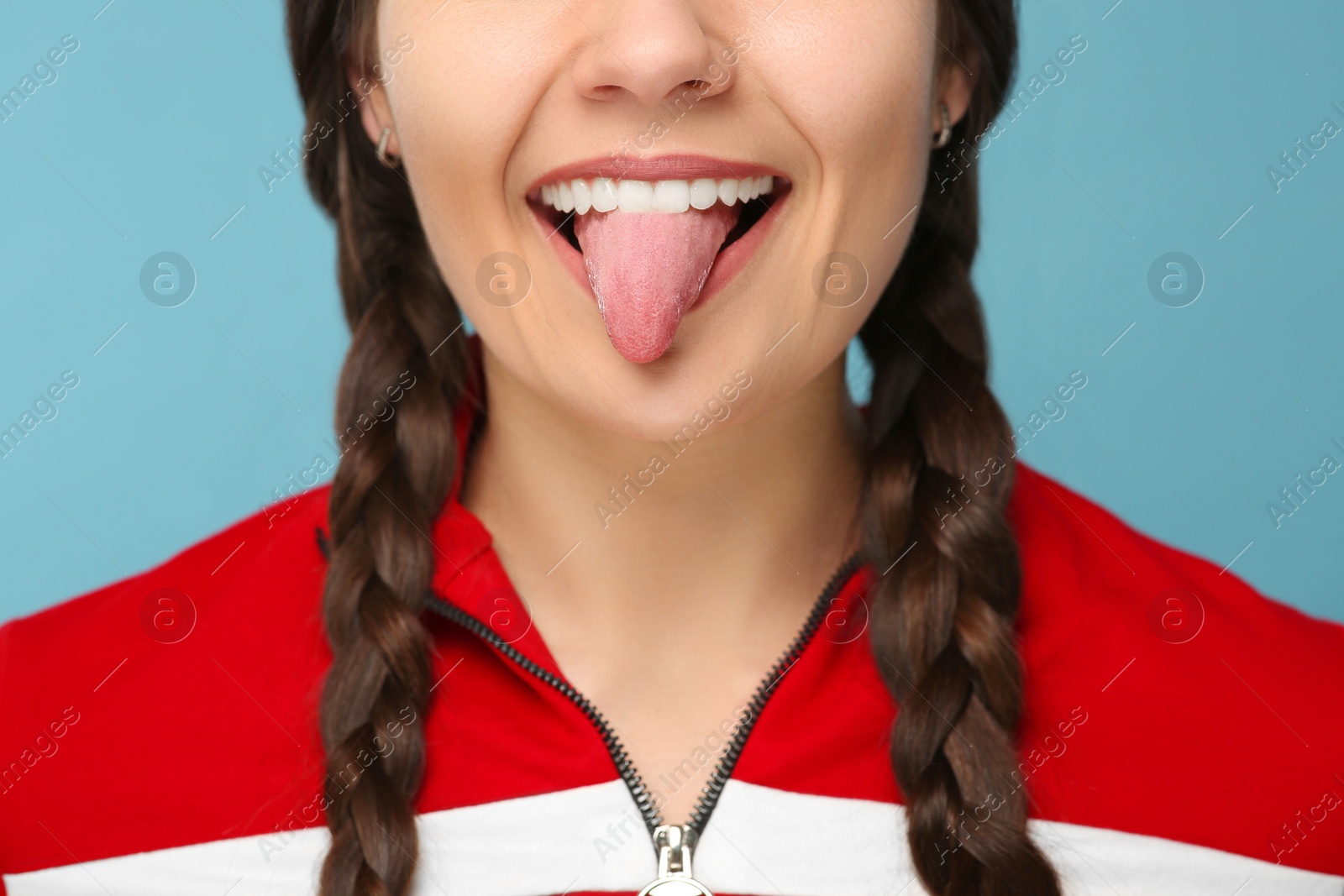 Photo of Happy young woman showing her tongue on light blue background, closeup