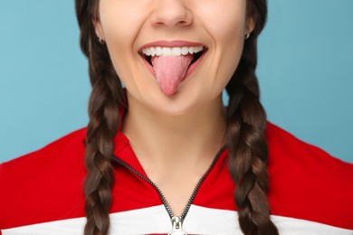 Happy young woman showing her tongue on light blue background, closeup