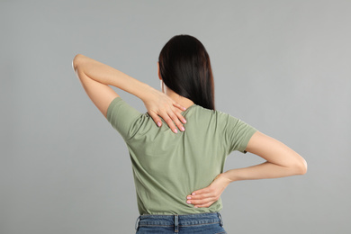 Woman suffering from pain in back on light grey background. Visiting orthopedist
