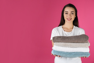 Photo of Happy young woman holding clean towels on color background, space for text. Laundry day