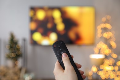 Photo of Woman with remote control in room decorated for Christmas, closeup