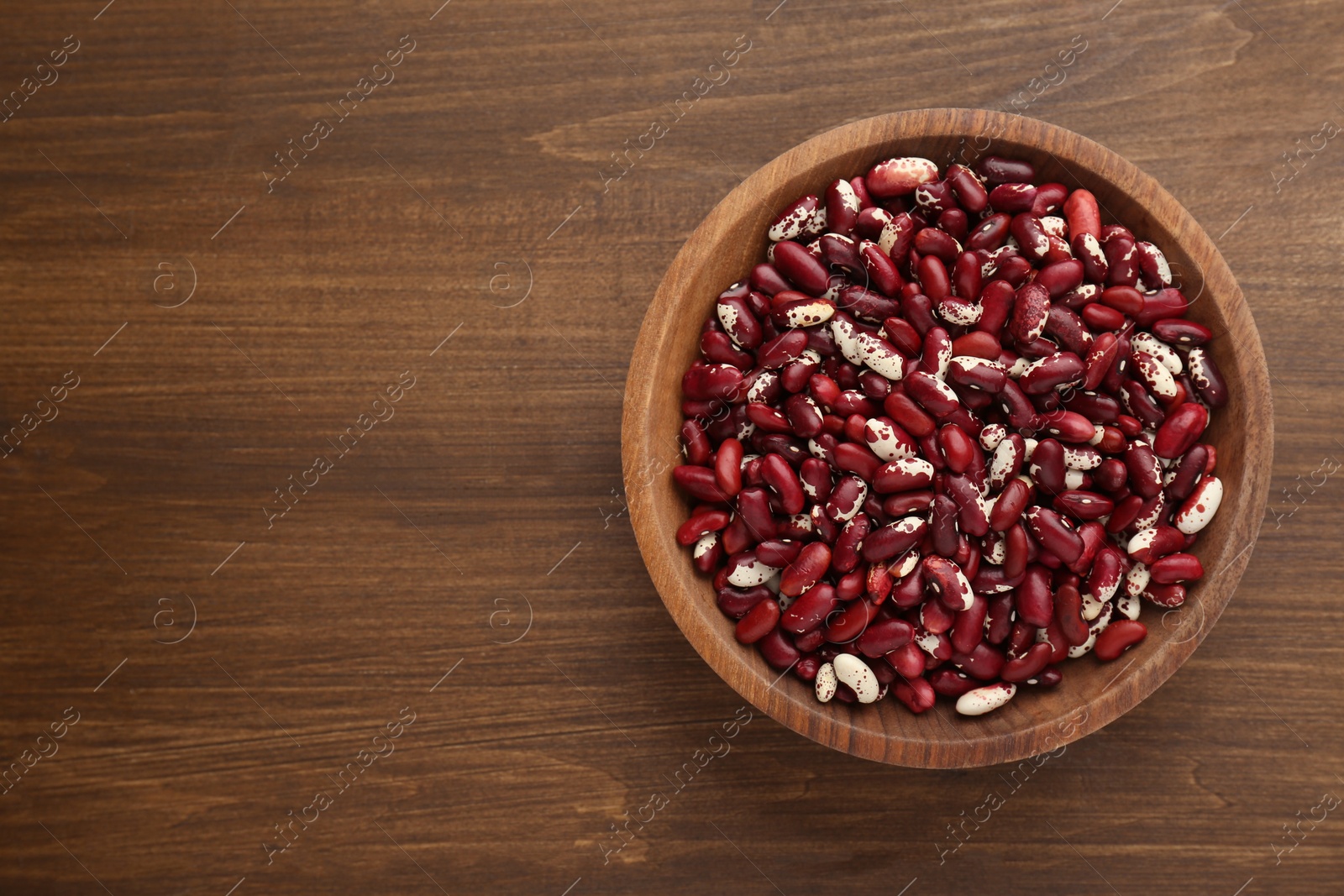 Photo of Bowl with dry kidney beans on wooden table, top view. Space for text