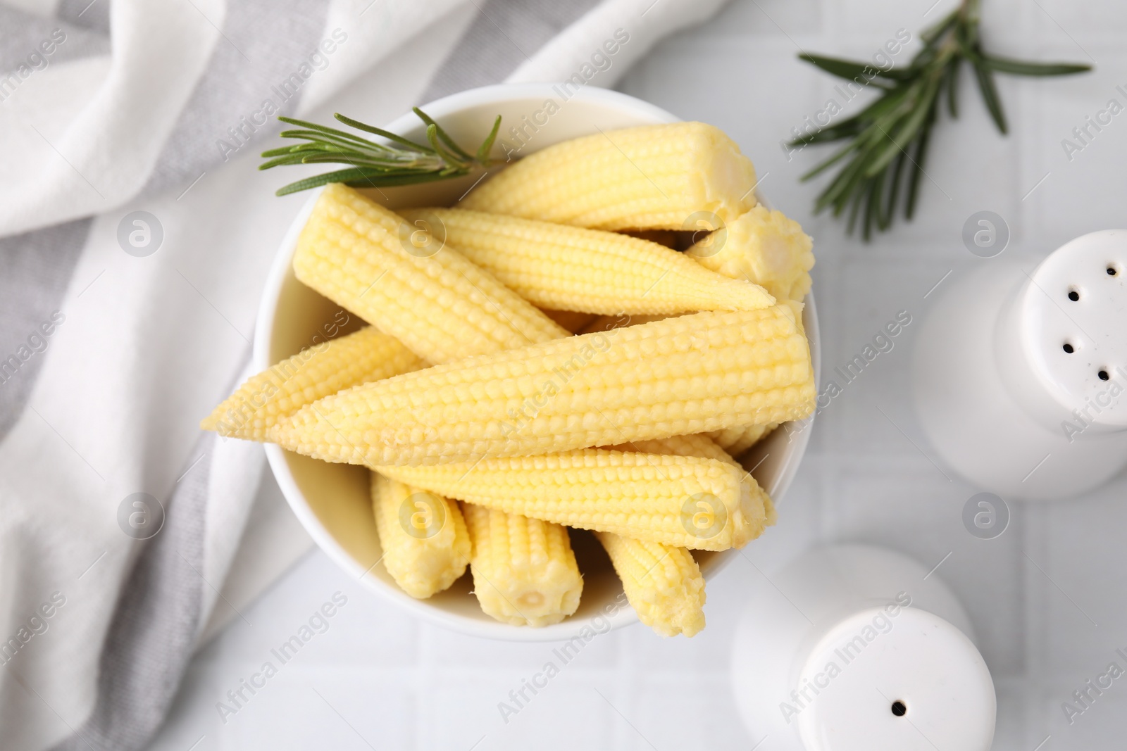 Photo of Tasty fresh yellow baby corns in bowl on white tiled table, top view