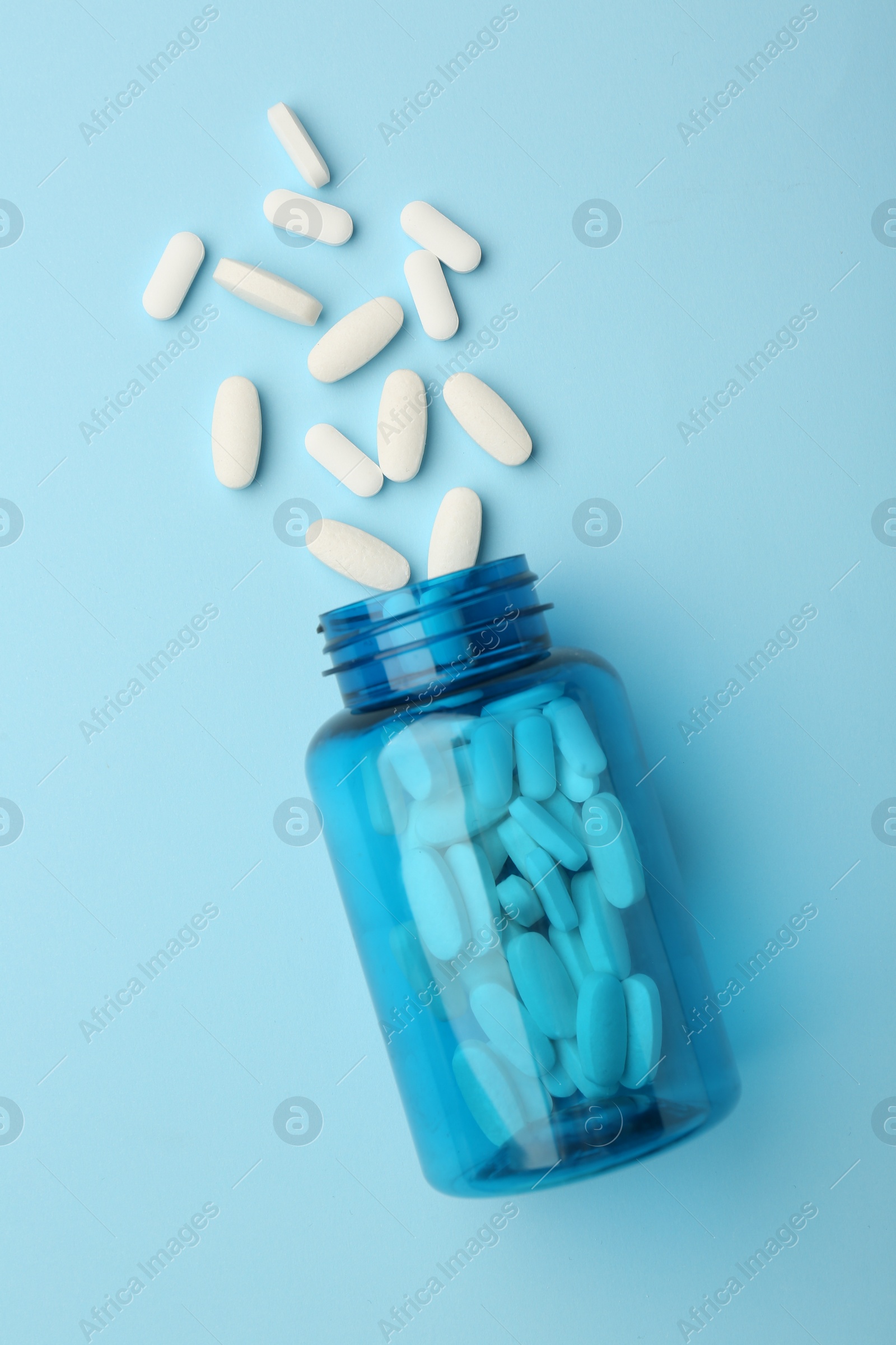 Photo of Vitamin pills and bottle on light blue background, top view