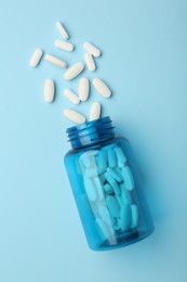 Vitamin pills and bottle on light blue background, top view