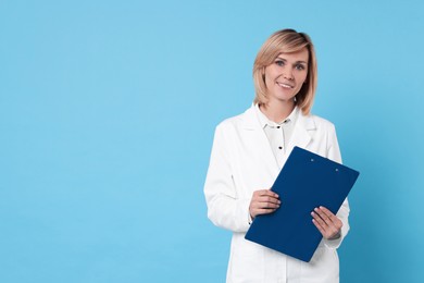 Photo of Smiling doctor with clipboard on light blue background. Space for text