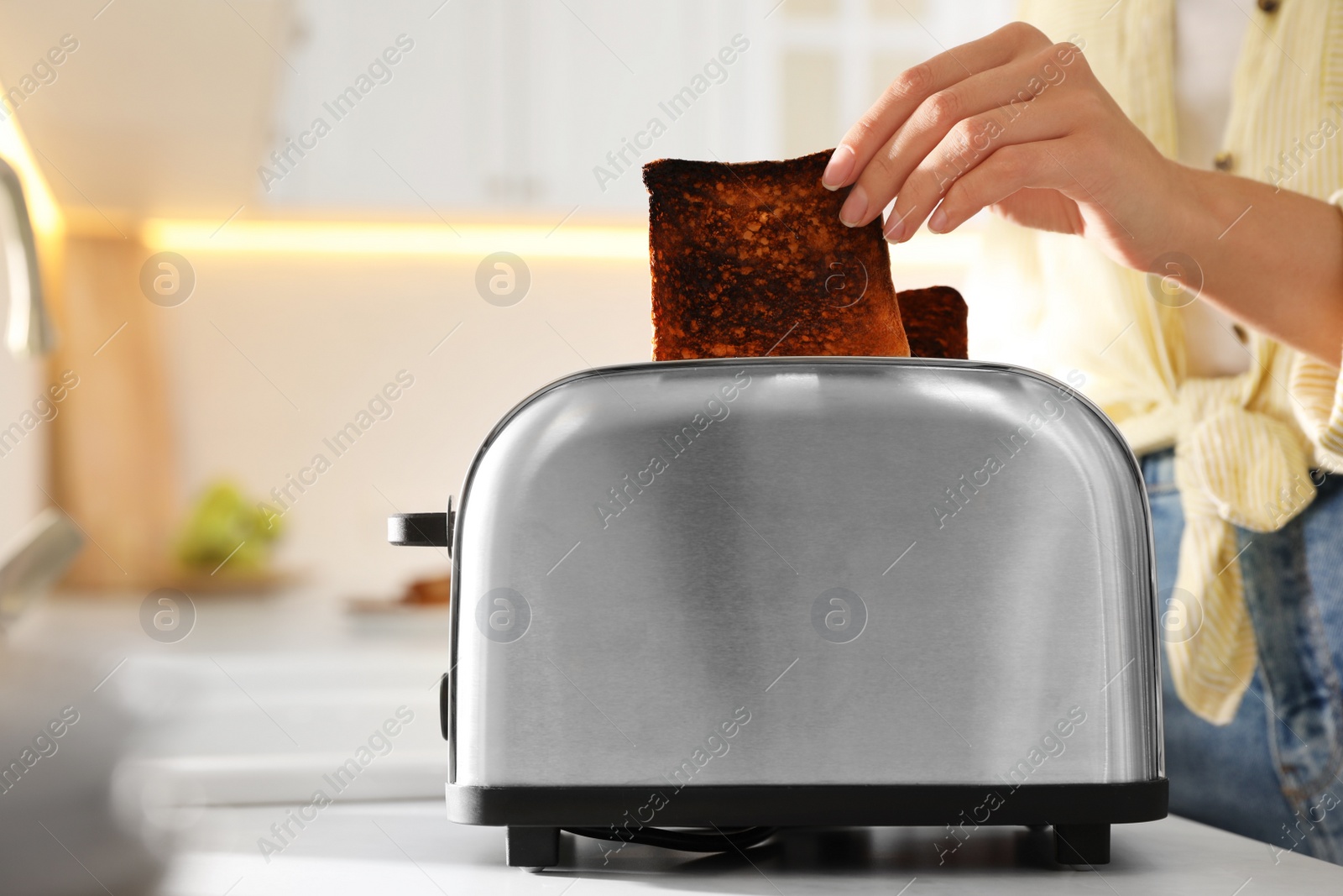 Photo of Woman taking slice of burnt bread from toaster in kitchen, closeup